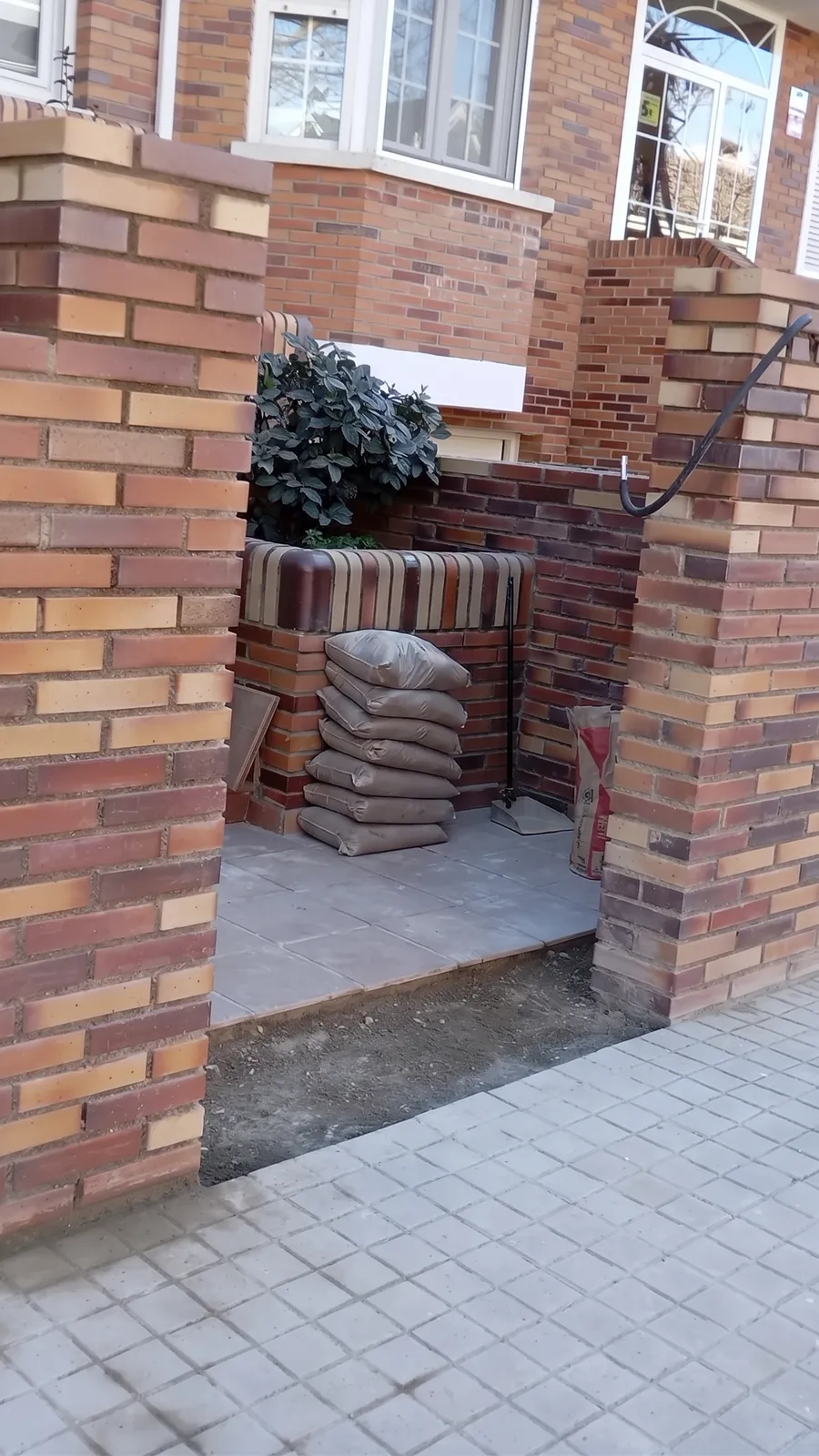 Acceso a una vivienda entre pilares de ladrillo bicolor, con jardinera de obra y solado nuevo