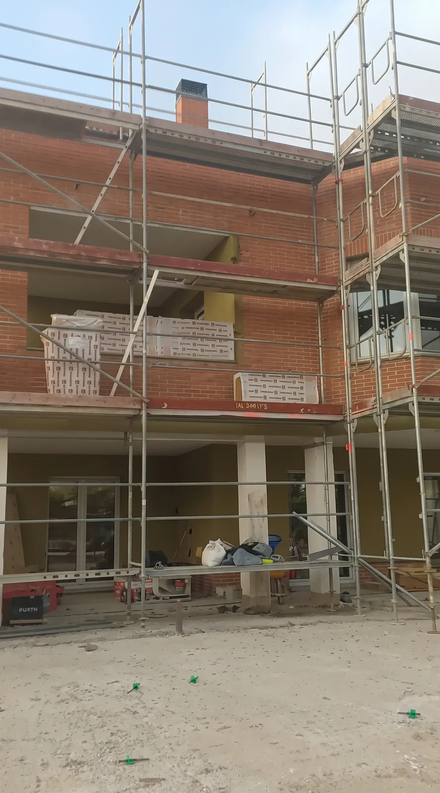 Fachada de ladrillo rojo de una vivienda con andamios y paquetes de aislamiento en los forjados