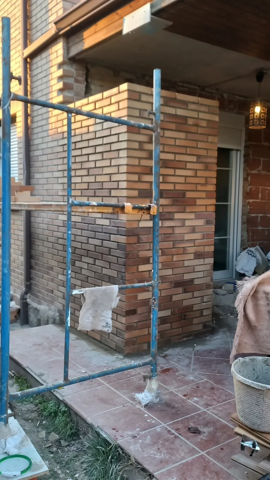 Fachada de ladrillo cara vista con andamio y terraza de baldosa cerámica