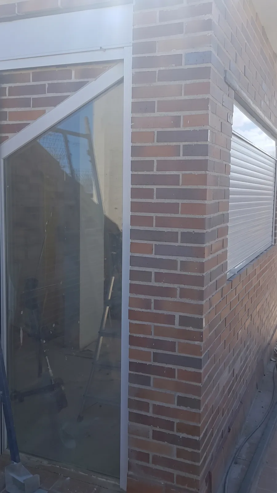 Esquina de fachada de ladrillo cara vista con ventanal de aluminio y persiana