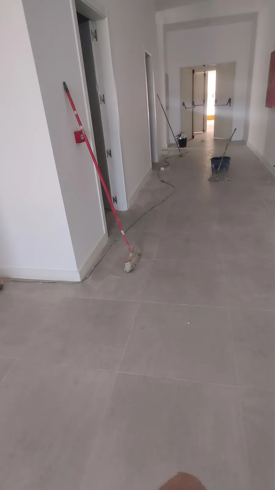 Pasillo con suelo de gres gris de gran formato recién colocado y puertas de emergencia al fondo